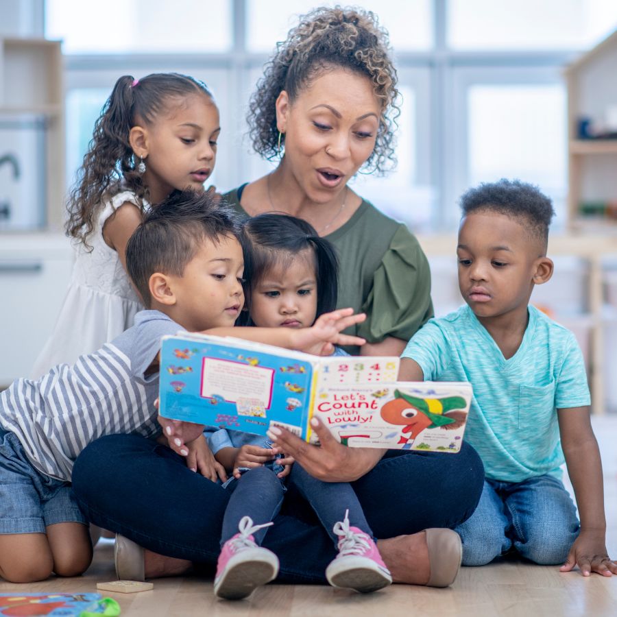 the teacher patiently reads book to a group of preschoolers