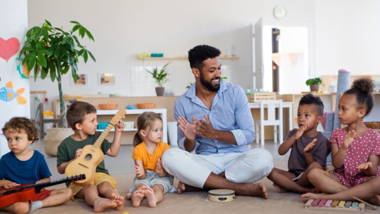 A male teacher jive with the little ones in playing instruments